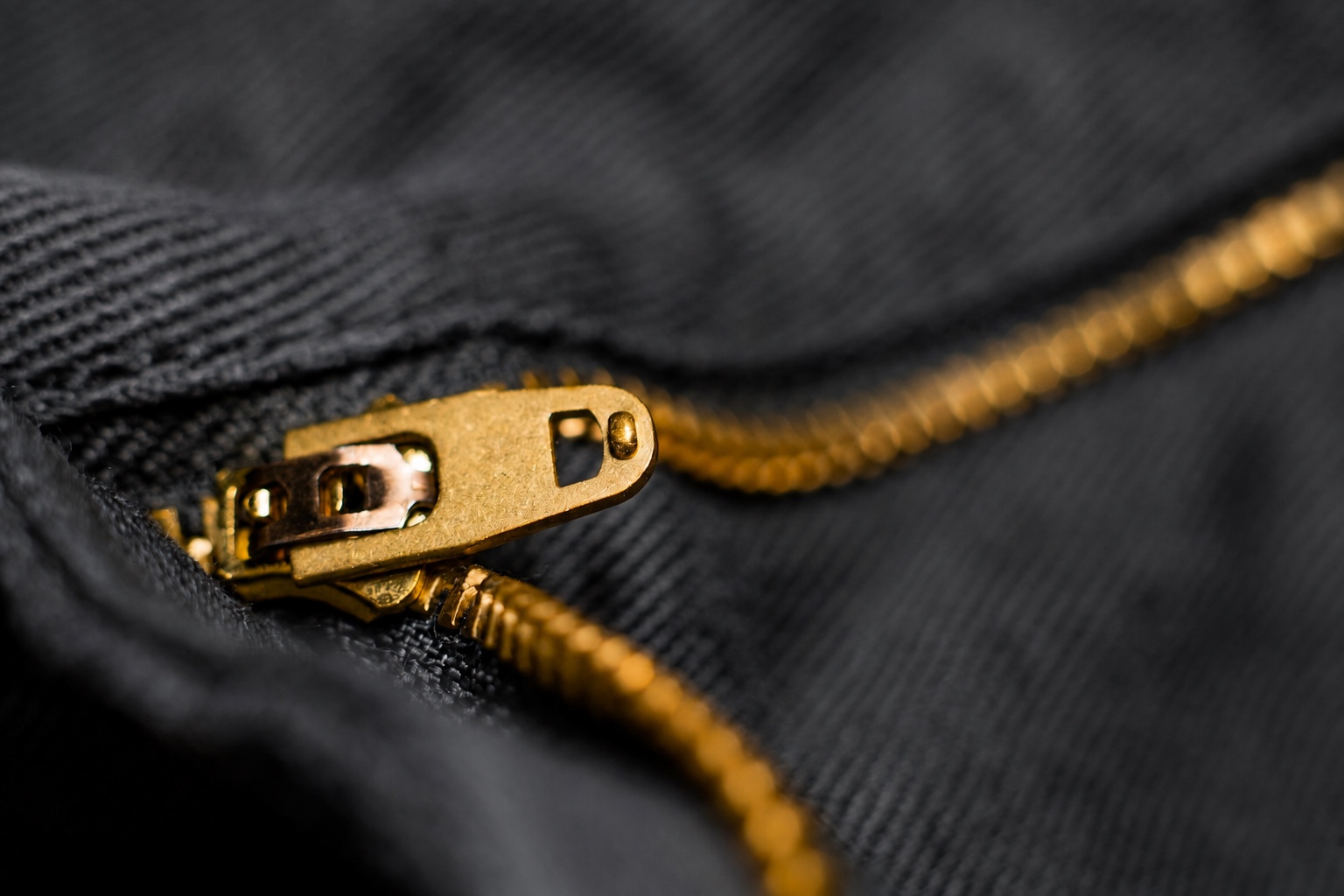 Gold-colored zipper slider and teeth against dark woven fabric