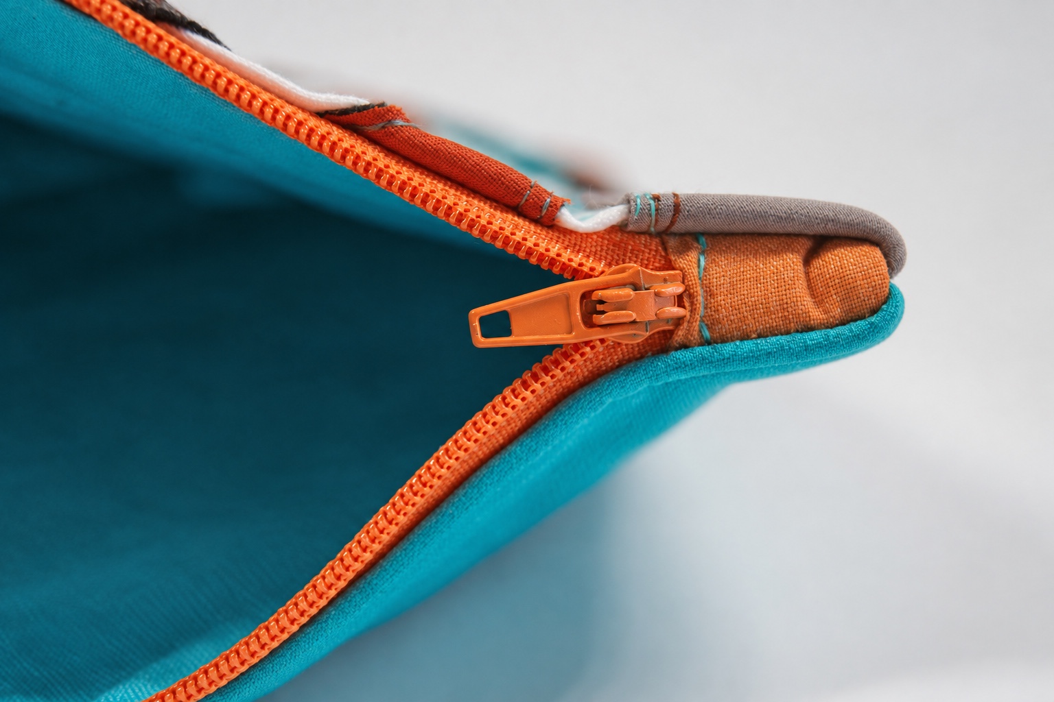 Orange coil zipper with visible slider and reinforced end on a turquoise fabric pouch