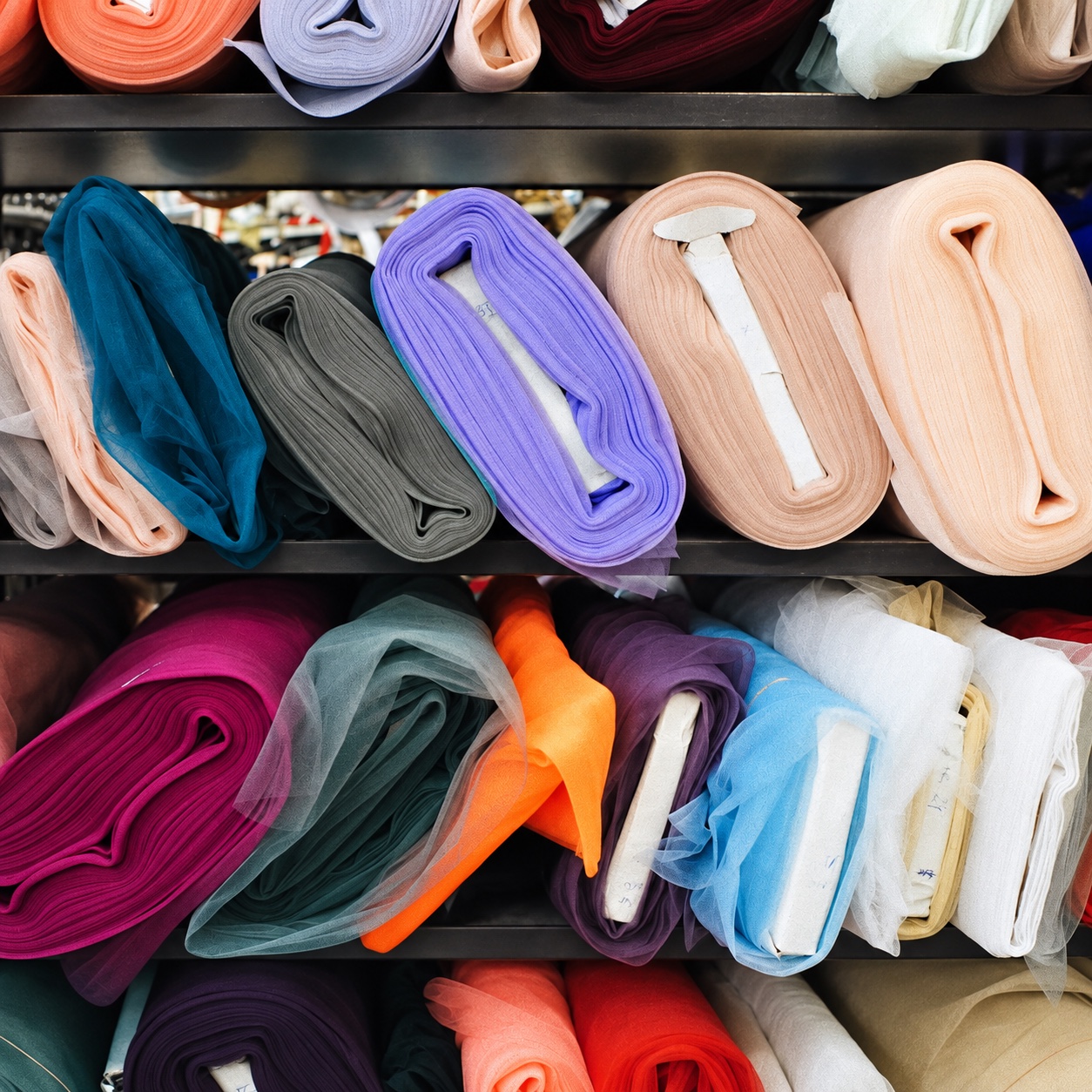 Different colored fabric rolls with cardboard cores arranged on dark shelves