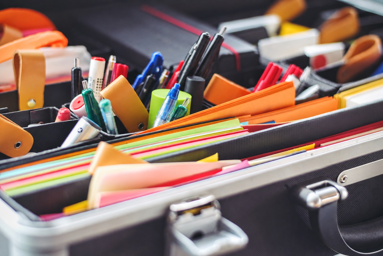 Pens and colored paper arranged in separate sections of an organizer case
