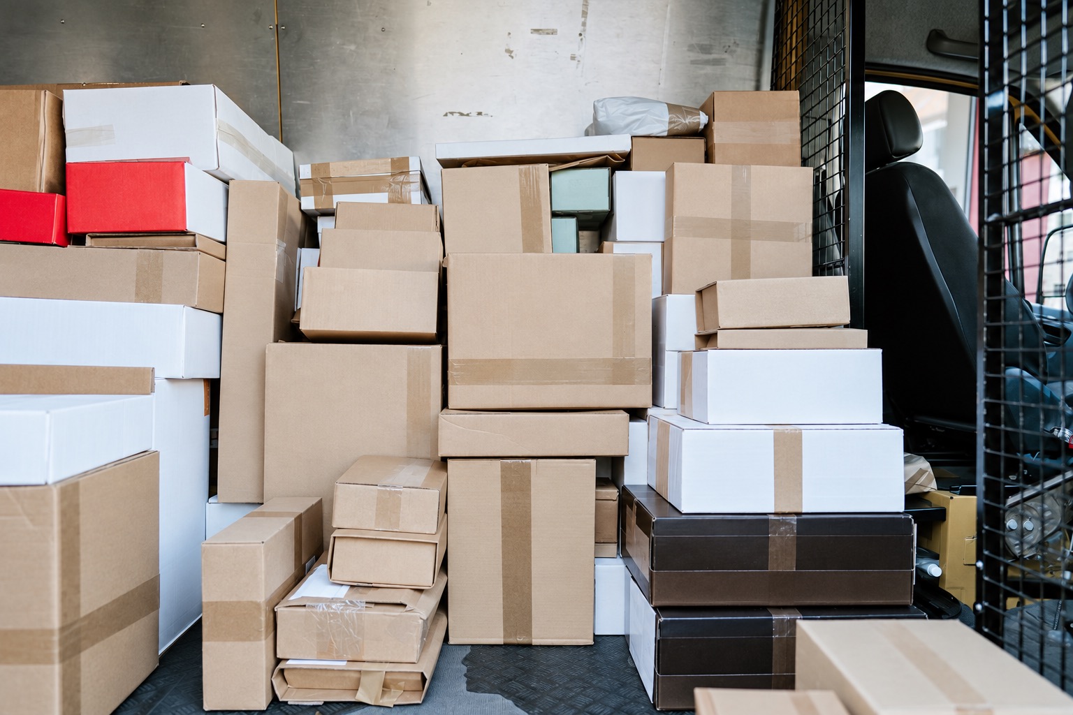 Closed cartons stacked inside a delivery van beside its mesh partition