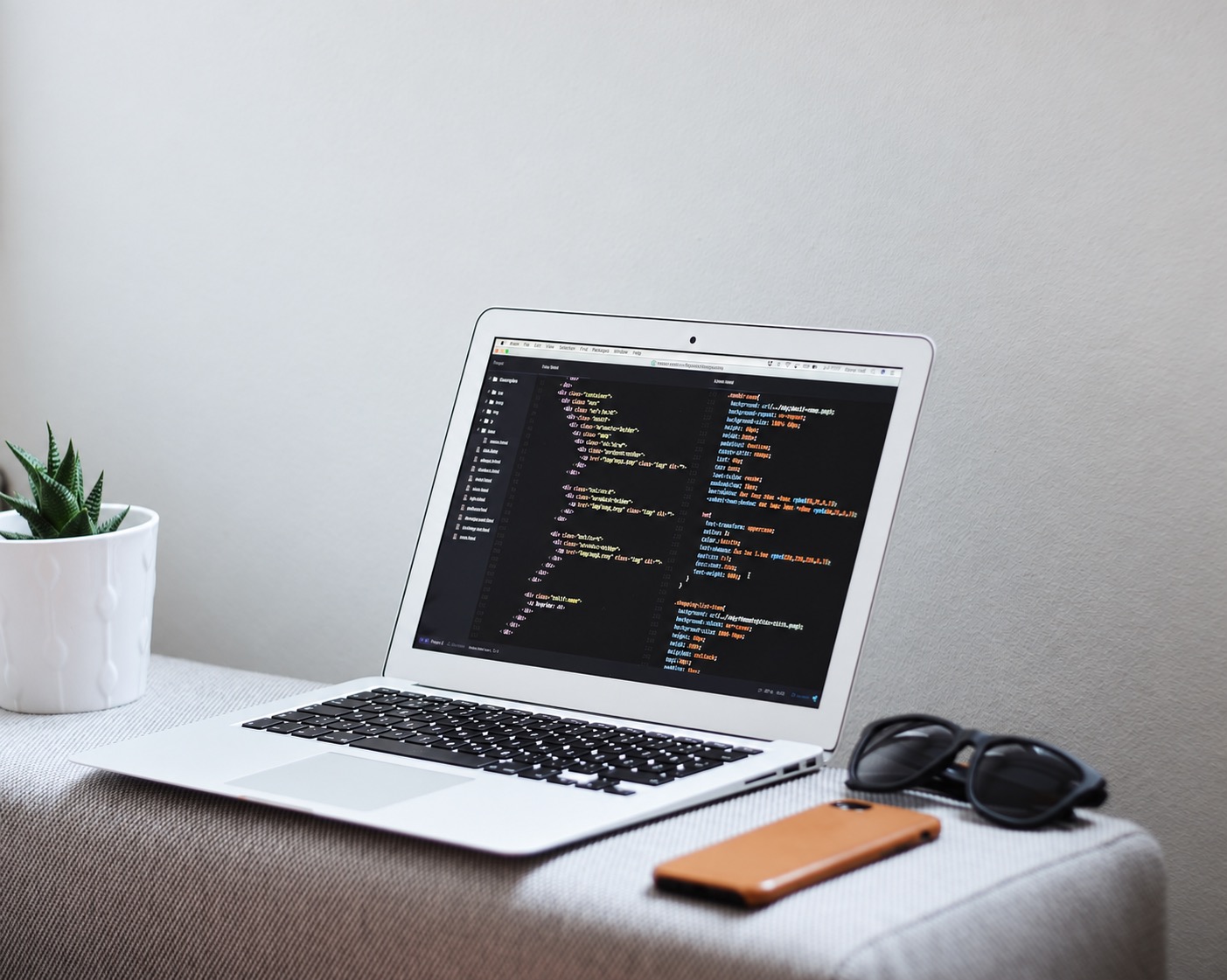 Laptop displaying code beside a plant, phone and glasses