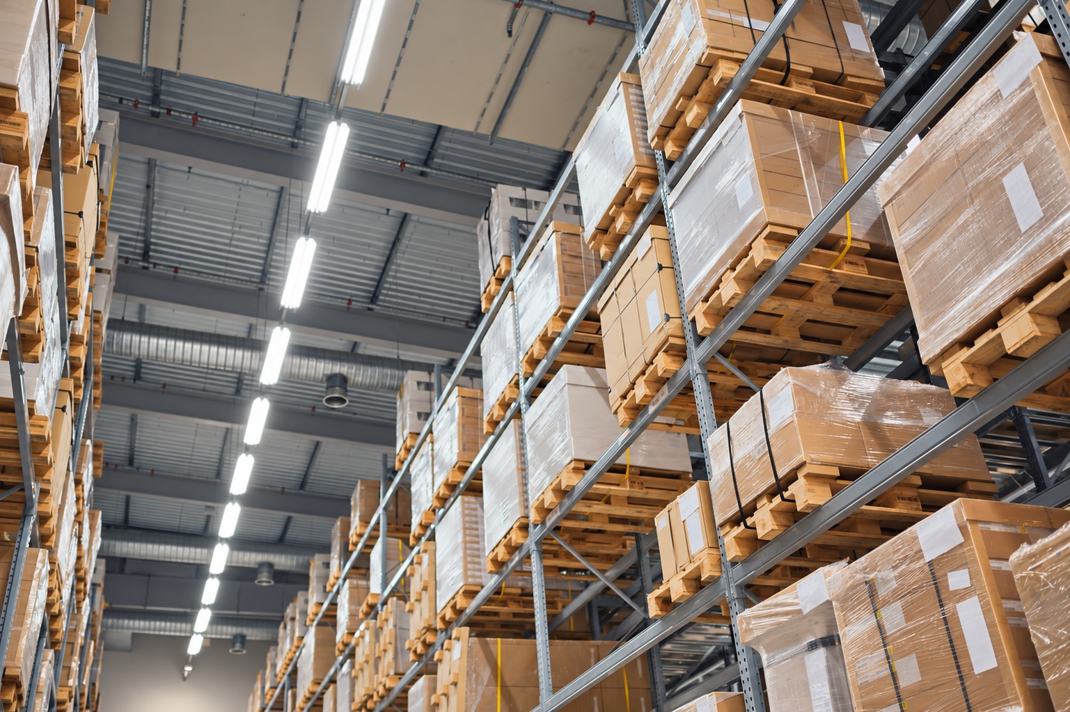 Shrink-wrapped cartons on supported pallets in a tall warehouse storage aisle