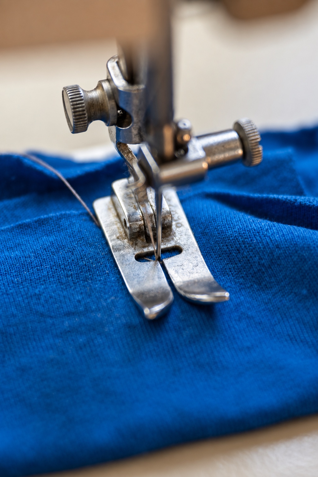Sewing machine needle and metal presser foot resting on blue fabric