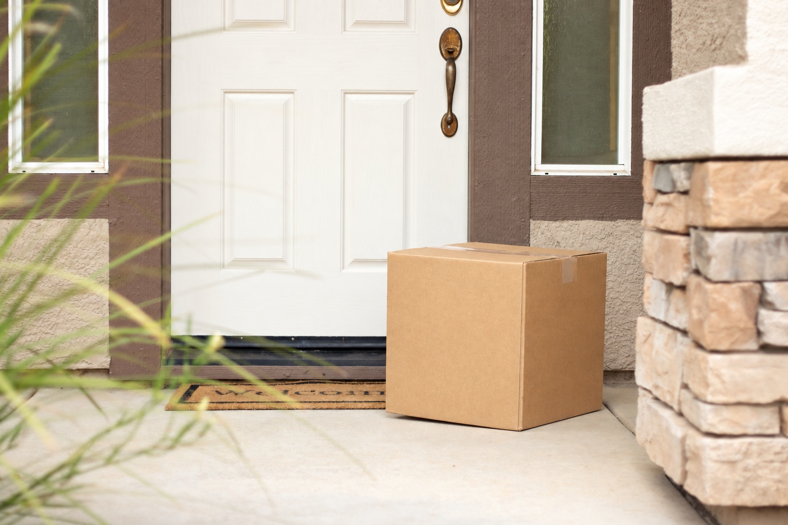 Plain cardboard carton resting on a porch beside closed front door