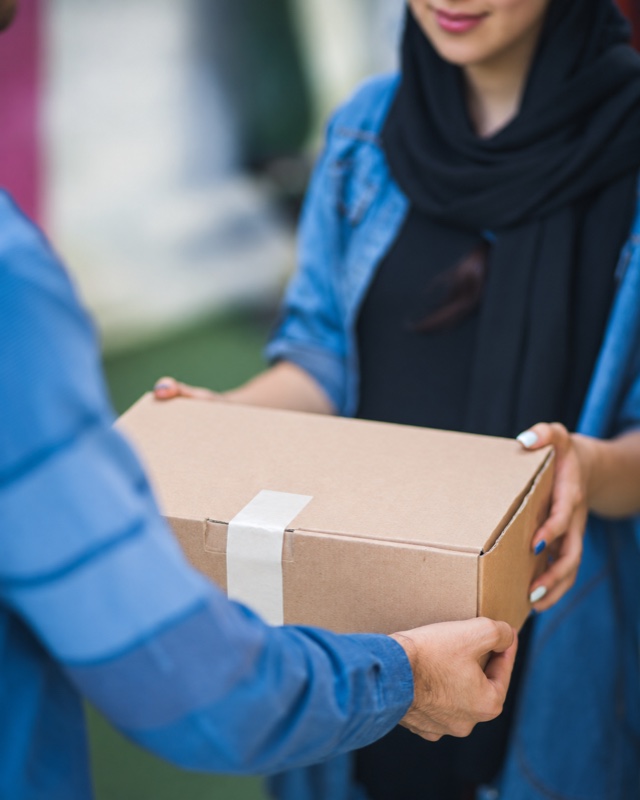 Two people supporting a sealed cardboard parcel during handoff