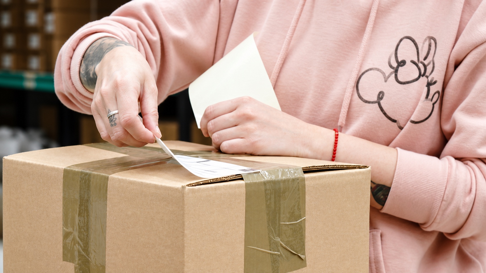 Hands applying an exterior label to the top of a taped cardboard carton