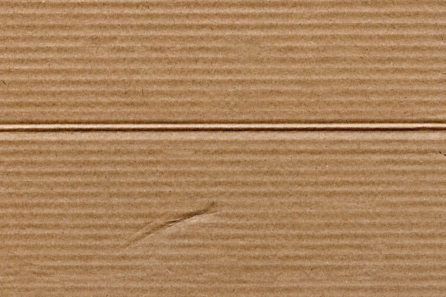 Close-up of brown corrugated cardboard with a scored crease and a small surface scuff