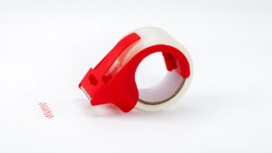 Red handheld dispenser with a roll of clear packing tape on a light background