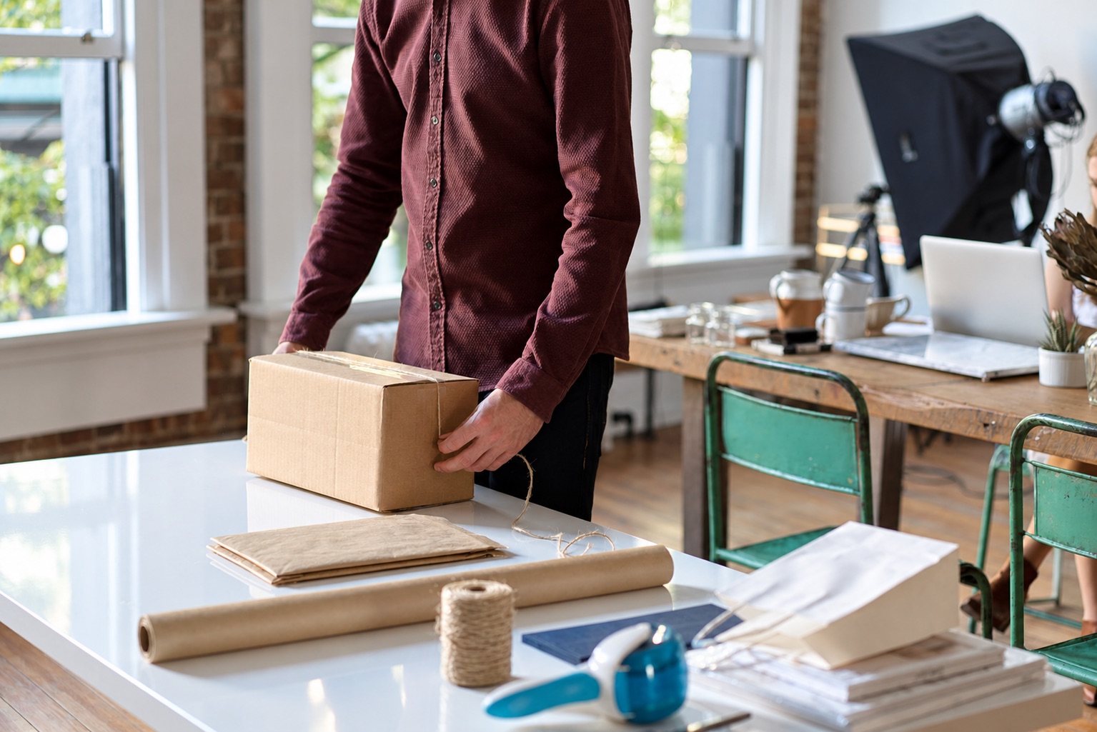 Person holding a sealed carton beside paper mailers and packing supplies