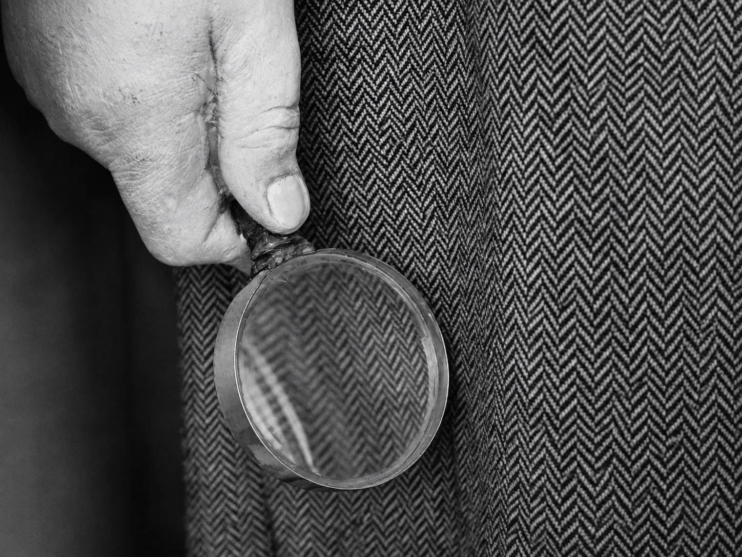 Hand holding a magnifier against herringbone fabric, illustrating return inspection detail