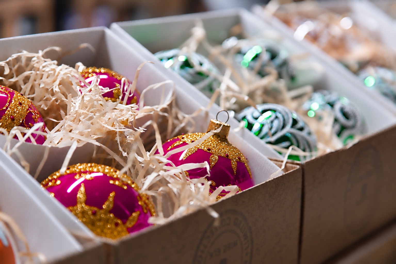 Magenta and green seasonal ornaments separated by cardboard dividers and paper cushioning