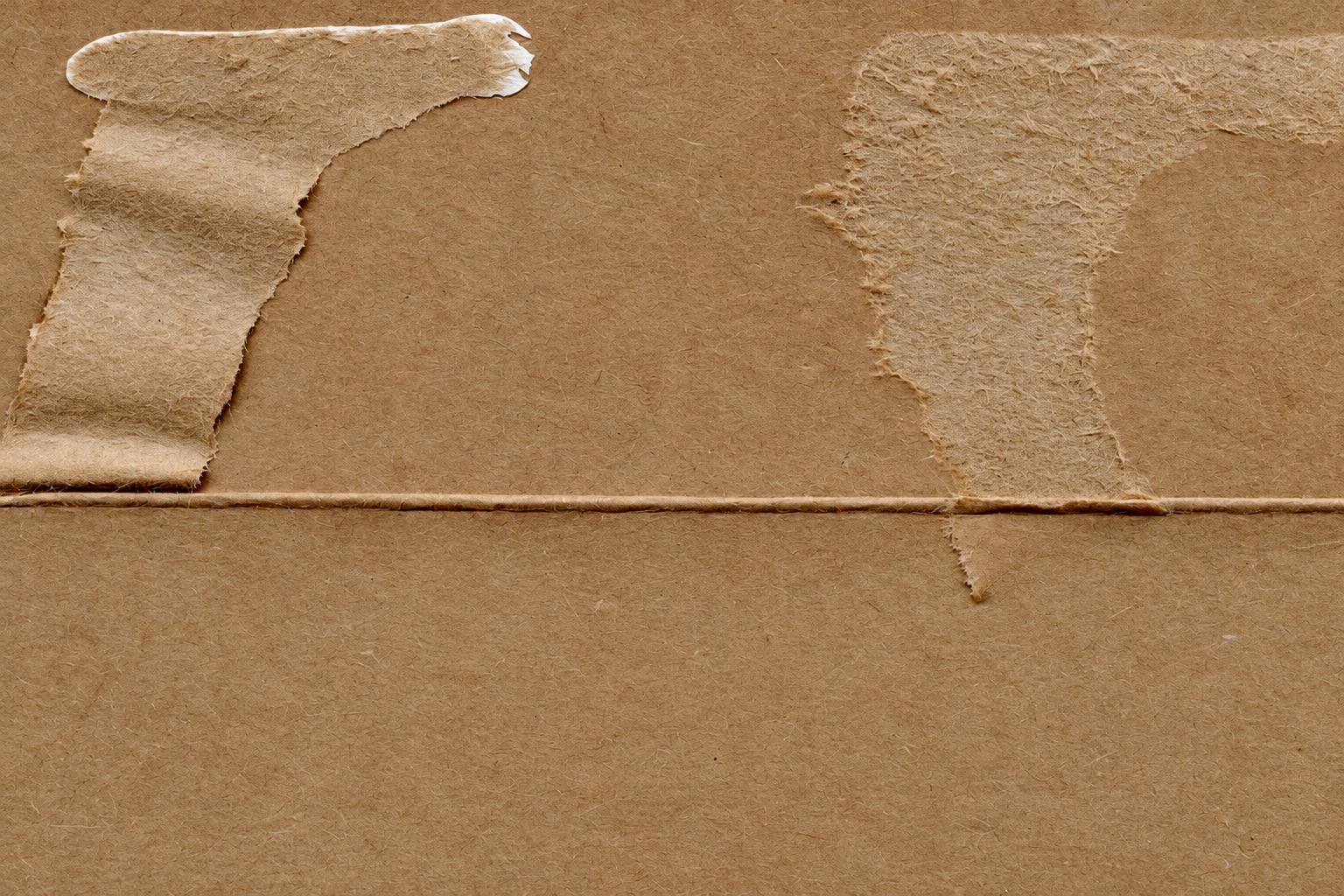 Close view of torn paper residue and a crease on brown cardboard
