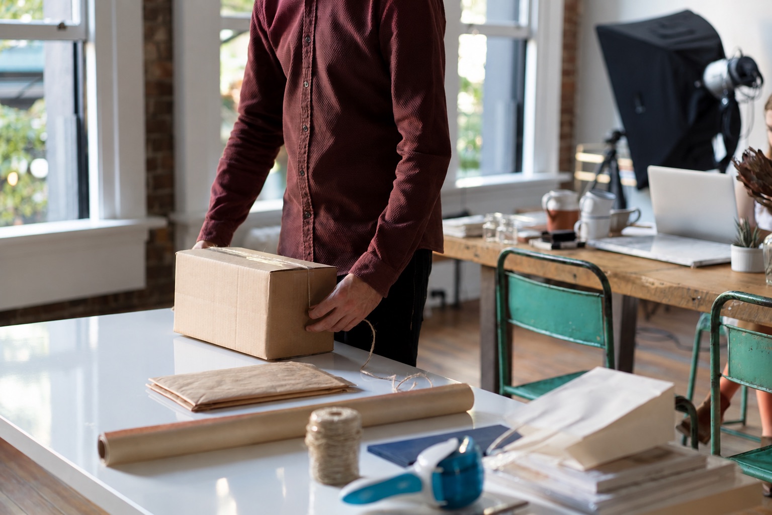 Person holding a closed carton beside paper mailers and packing materials