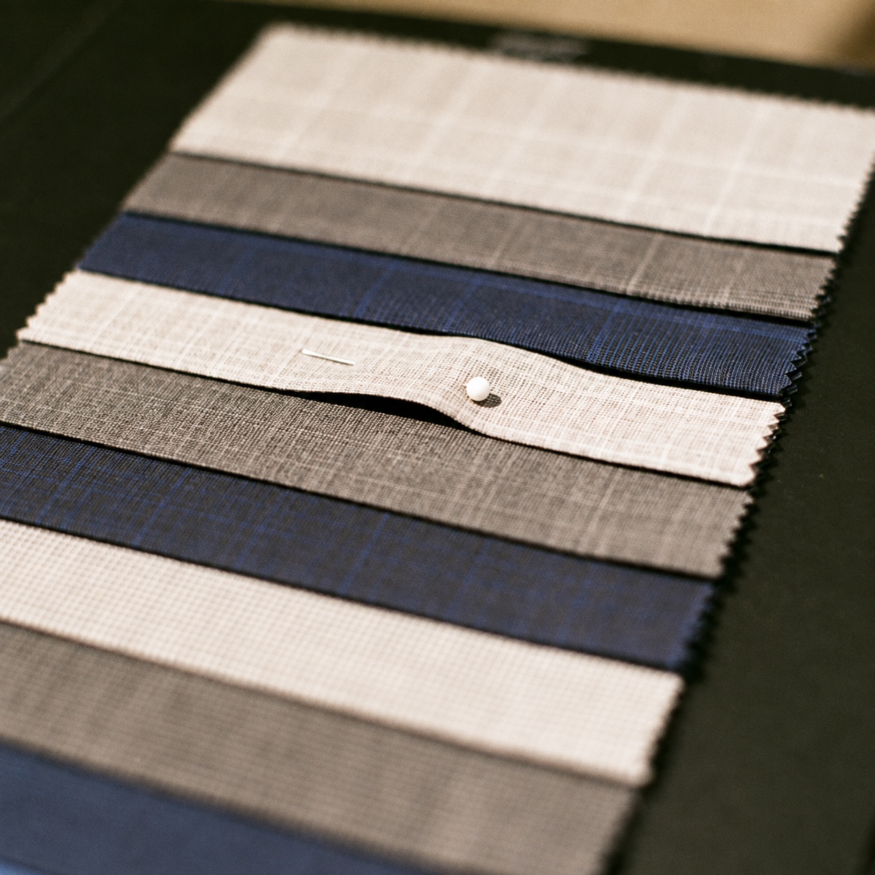 Navy beige and gray fabric swatches on a sample book with a pin