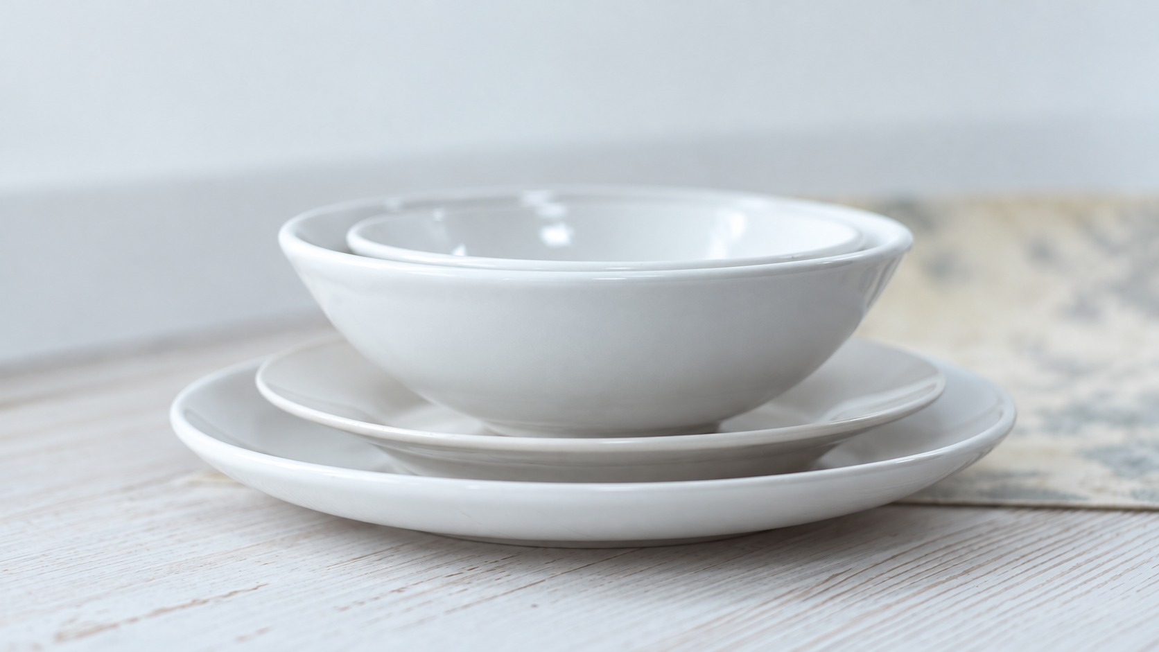 Stacked white ceramic tableware on a pale wooden table