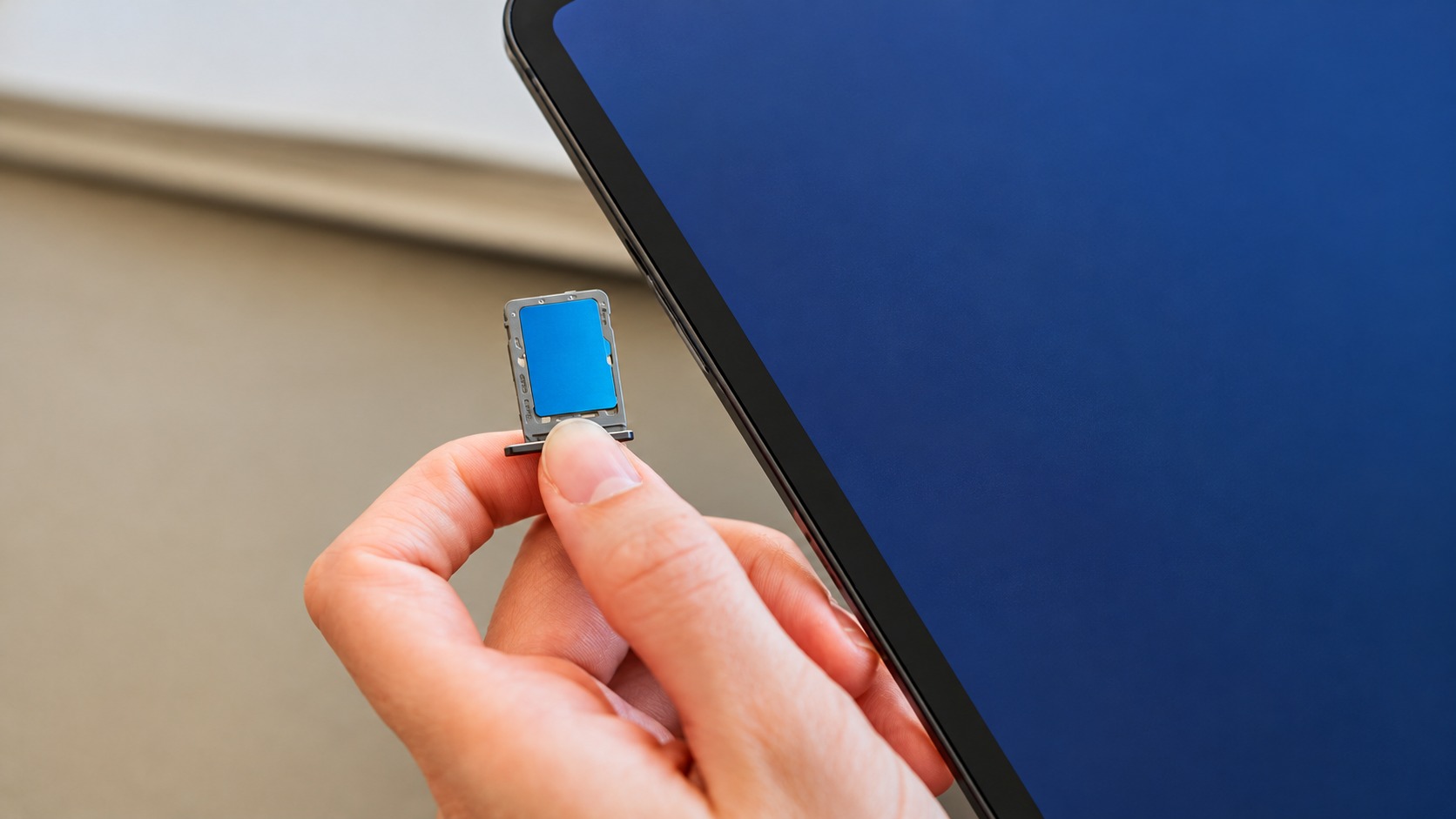 Hand holding a blue storage card beside a tablet with a plain blue screen