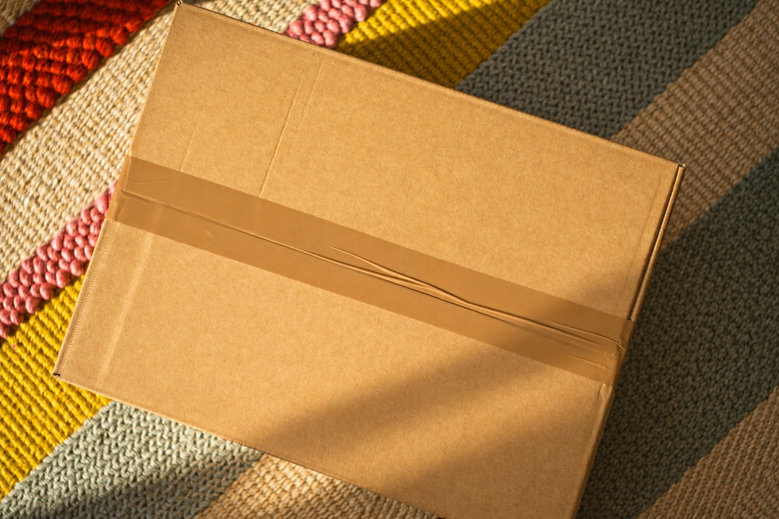 A single cardboard parcel taped shut on a colorful woven rug