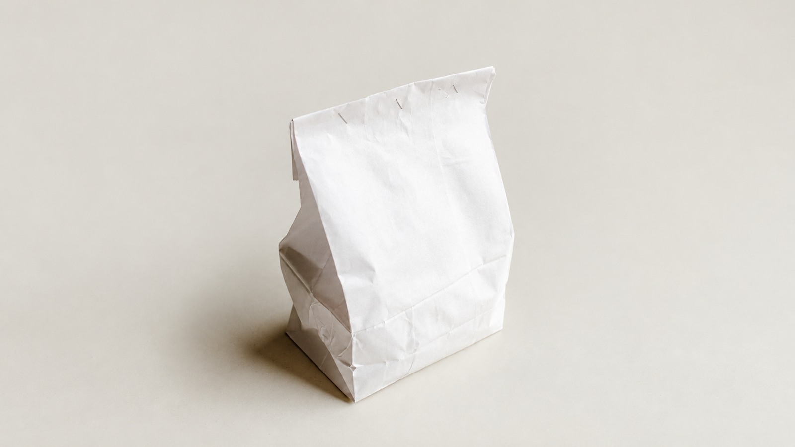 A plain white paper bag with visible folds on a cream surface