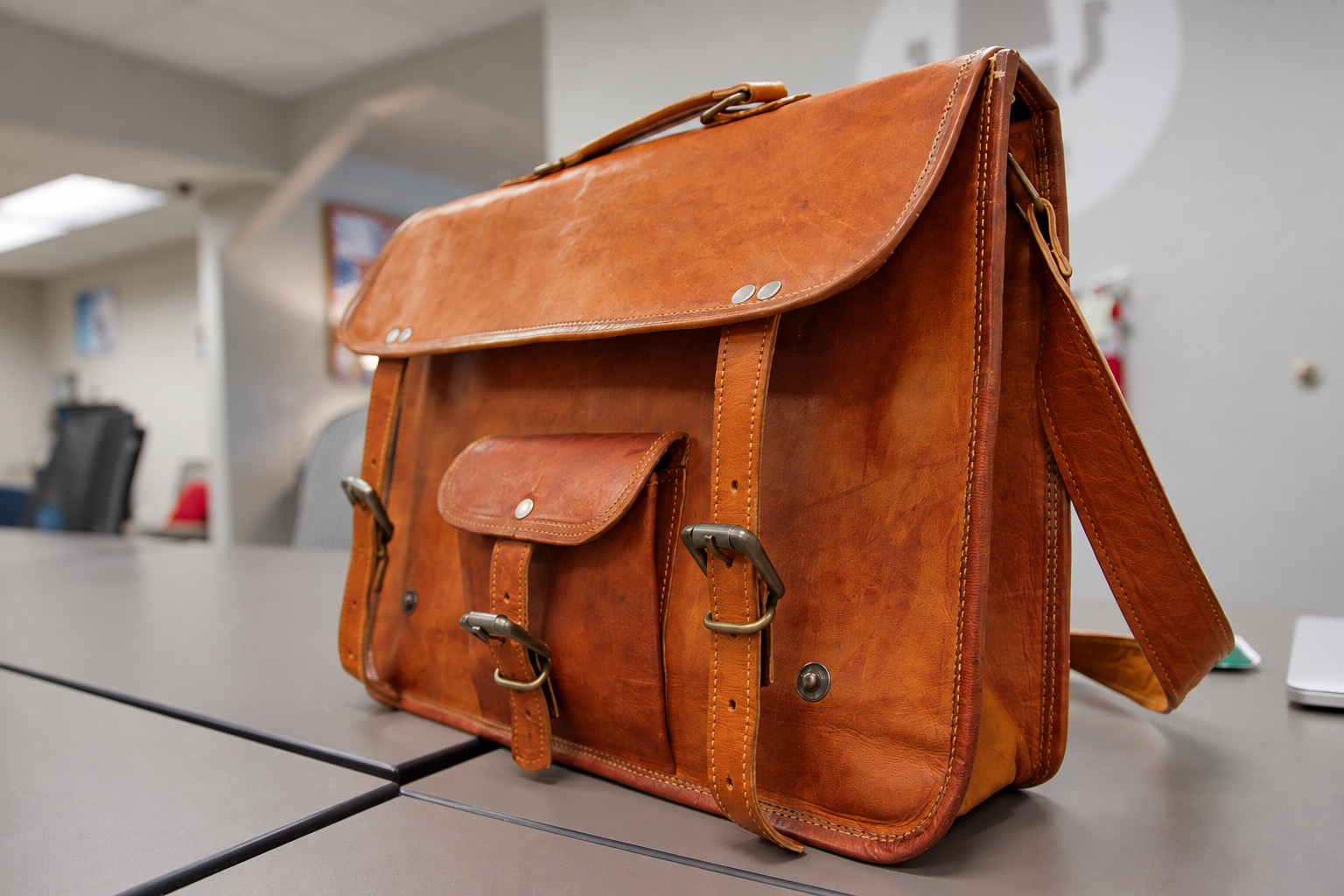 Closed brown satchel showing exterior pockets and buckles but not the interior compartments