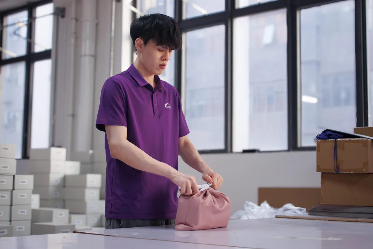 A person finishing a drawstring pouch at a warehouse packing station